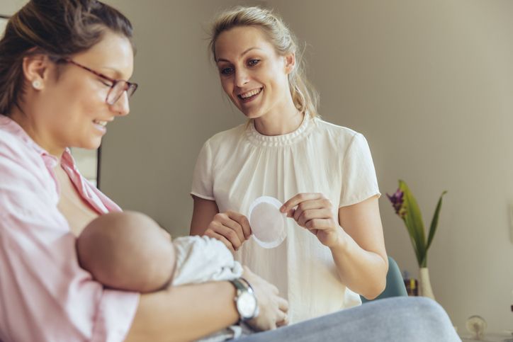 Mom breastfeeding while woman shows her a breast pad